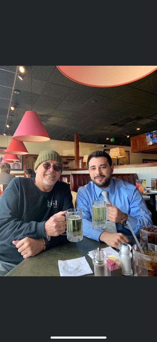 Two friends are smiling and raising their mugs in a lively restaurant setting.
