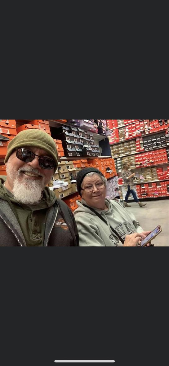 A couple is smiling and sitting together while surrounded by rows of vibrant shoe boxes.