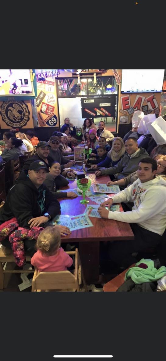Large group of family members seated around tables sharing food and laughter on a busy evening.