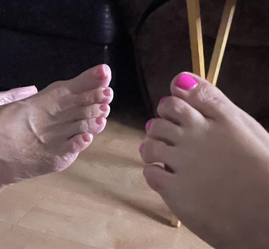Two pairs of feet with colorful nail polish rest on a wooden floor, enhancing a relaxed vibe.