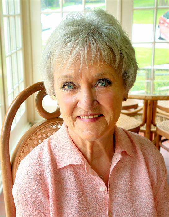 Bright sunlight fills the room as an elderly woman smiles gently while sitting.