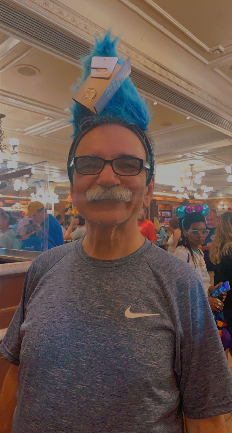 An older man wearing blue hair and sunglasses enjoys a festive atmosphere full of activity.