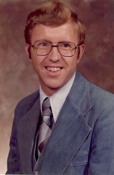 Man dressed in a blue suit and tie smiles warmly for a formal portrait in a studio.