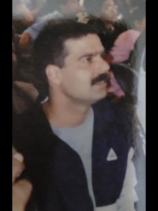 A man wearing a navy jacket appears focused and alert in a crowded area, likely during daylight.