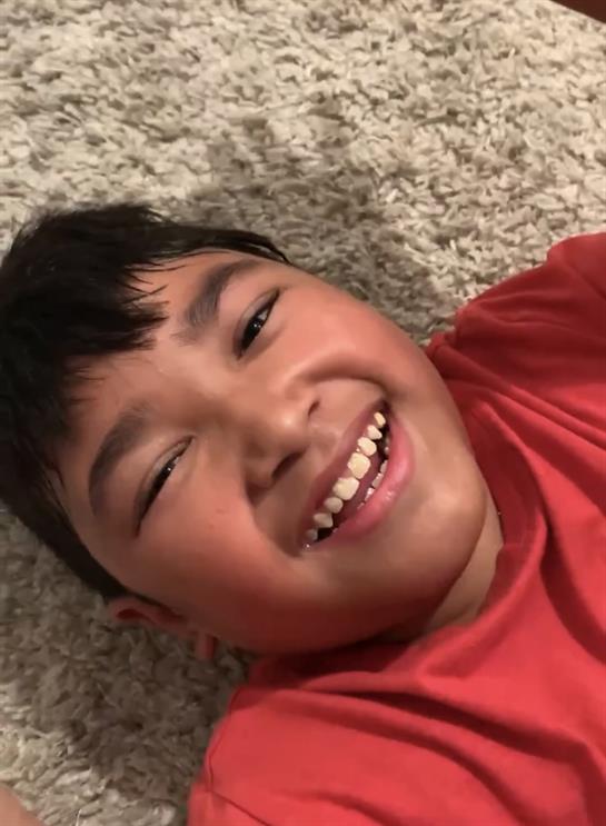 A joyful boy with a big smile relaxes on a cozy carpet, enjoying a carefree afternoon.