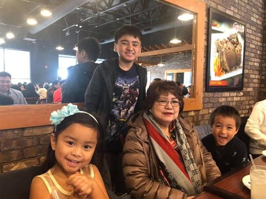 Children pose happily with their grandmother during a lunch outing at a cozy restaurant.