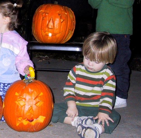 Two children engage in Halloween festivities, showcasing carved pumpkins in the evening light.