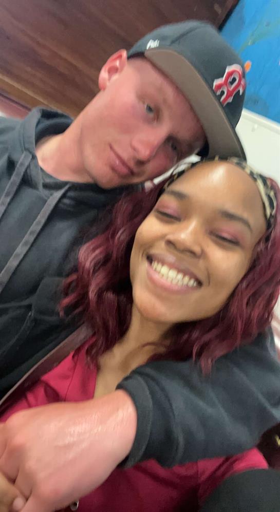 Two young individuals share a cheerful smile while posing closely at a social event indoors.