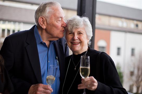 Smiling elderly couple enjoys a romantic kiss while holding drinks in celebration together.