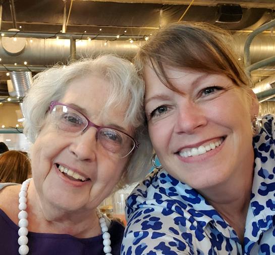 Two women smile broadly while enjoying time together at a lively restaurant setting.