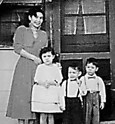 Kids in vintage clothes stand with a smiling woman at a doorway, enjoying the moment.