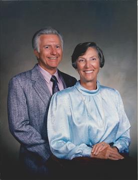 A couple dressed in formal clothing stands together, radiating joy and warmth indoors.