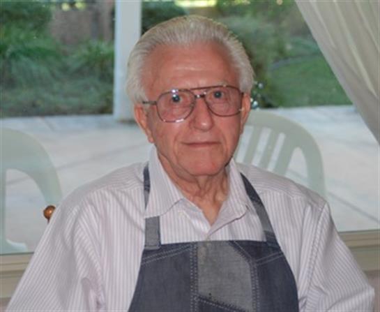 Elderly man in glasses and apron relaxes at a table with serene nature views.