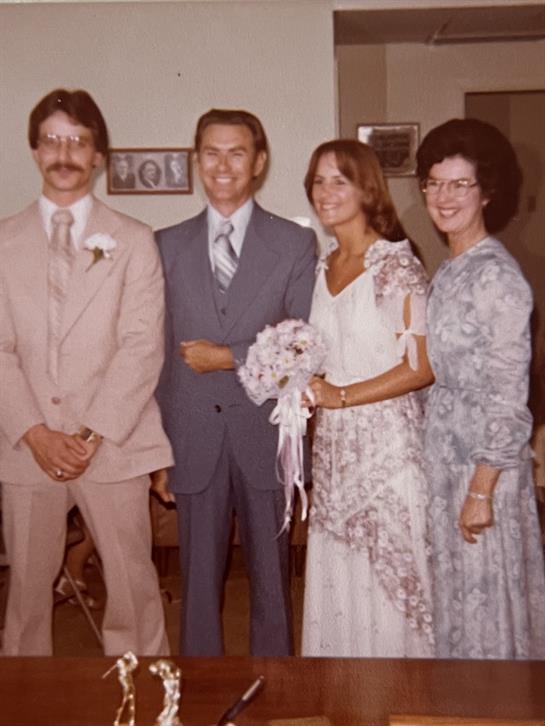 A wedding couple poses with family members in a warm, nostalgic indoor environment from the 1970s.
