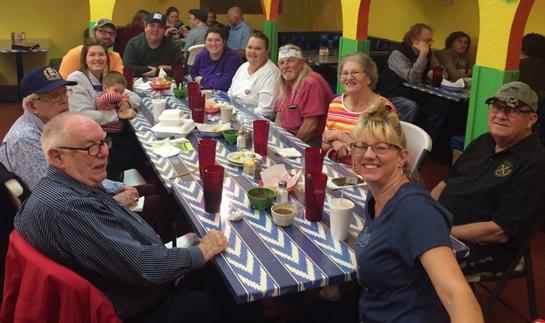 Group of friends and family relax and share food at a lively restaurant with colorful decor.