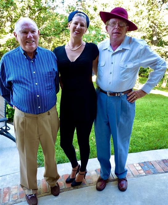 Three people are smiling together in a sunny, vibrant green outdoor setting.