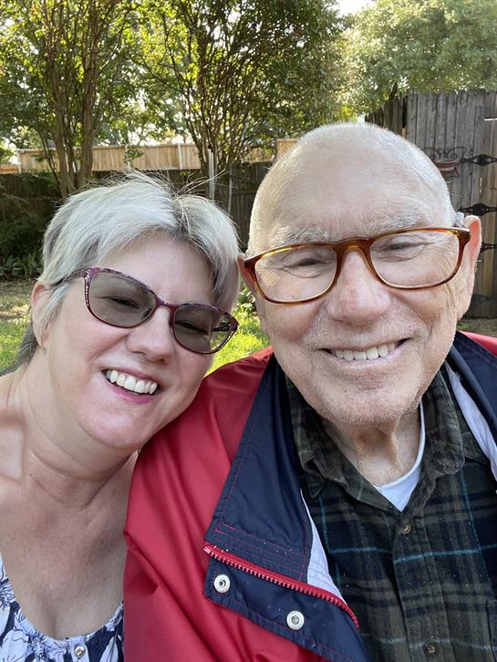 Two people beam with joy as they pose closely together in a bright garden under sunlight.