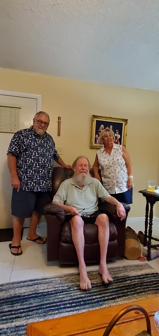 Two friends stand beside a mutual acquaintance in a bright room filled with warmth.