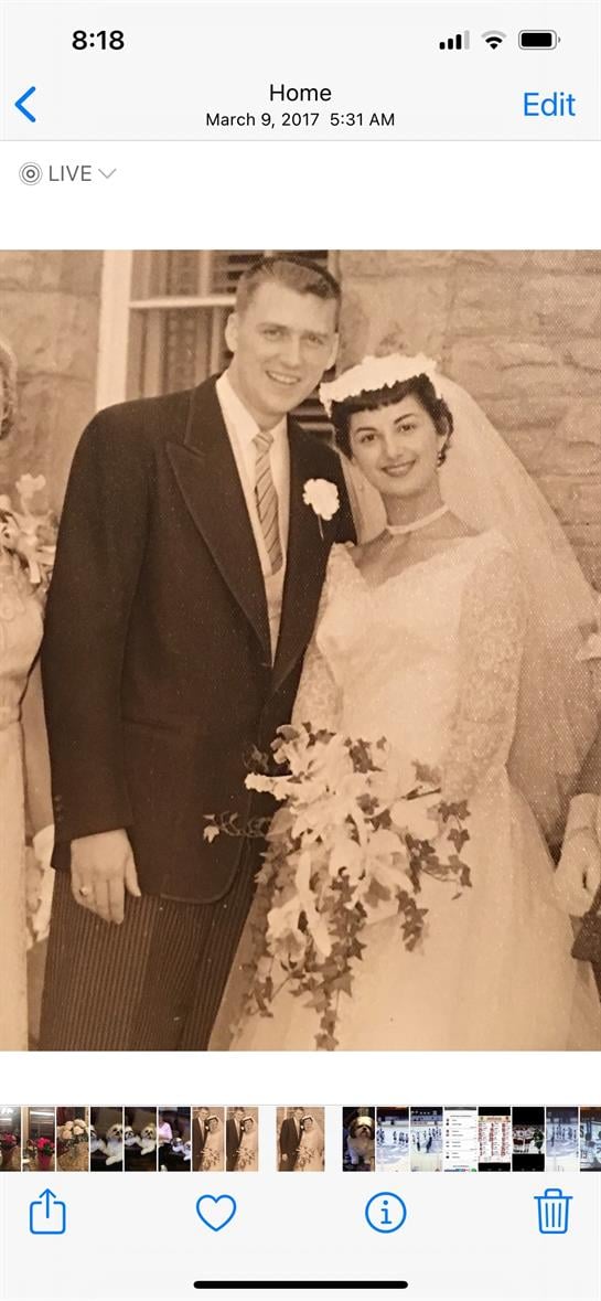 A newlywed couple stands smiling among family and friends in an indoor celebration setting.