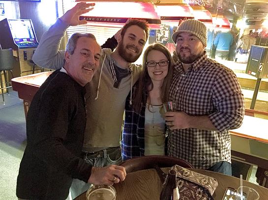 Group of friends smiles and poses with drinks at a vibrant bar during a relaxed summer night.