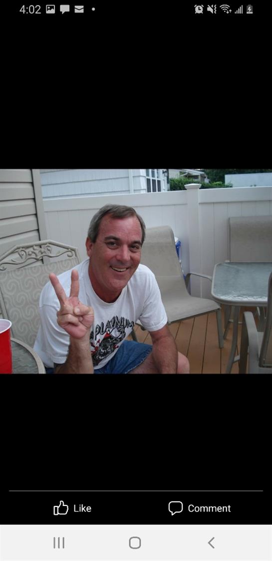 A cheerful man shows a peace sign while enjoying a summer gathering on a patio.