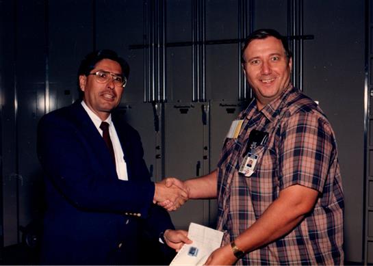 Men in formal wear shake hands, symbolizing partnership in an office setting.