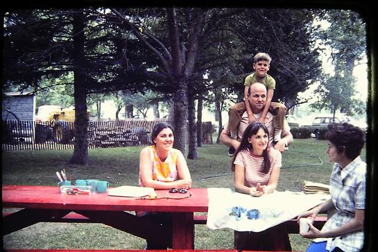 Friends gather around a table in a park, engaging in conversation and enjoying outdoor activities.