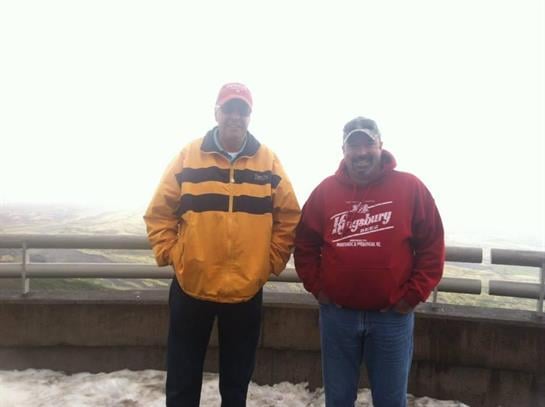 Two men in bright jackets pose in a foggy, cold high-altitude setting.