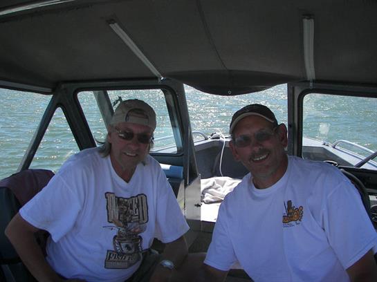 Two men smile while seated on a boat, enjoying their time together under clear skies.