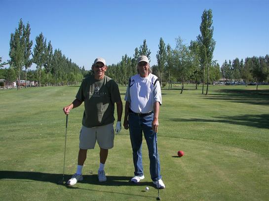 Two friends stand on a green golf course, smiling and ready to tee off on a sunny day.