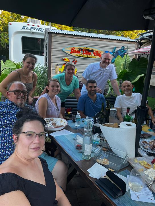 Friends celebrate together around a table filled with food and drinks in a lush, tropical setting.