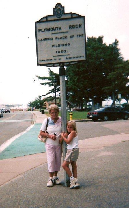 Two individuals stand next to a historic sign at Plymouth Rock, enjoying a summer visit.