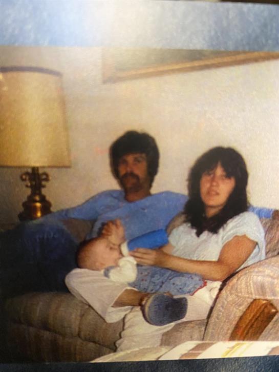 A couple sits together on a couch, holding a baby in a comfortable living room.