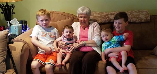 Grandmother sits with her four grandchildren, sharing smiles and laughter in a warm living space.