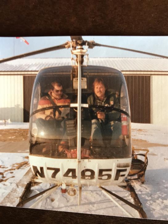 Two pilots prepare for takeoff in a helicopter at a snowy landing area on a winter day.