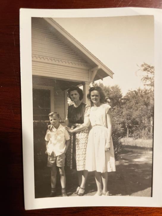 Family members smile together on a sunny day, standing outside their house surrounded by nature.