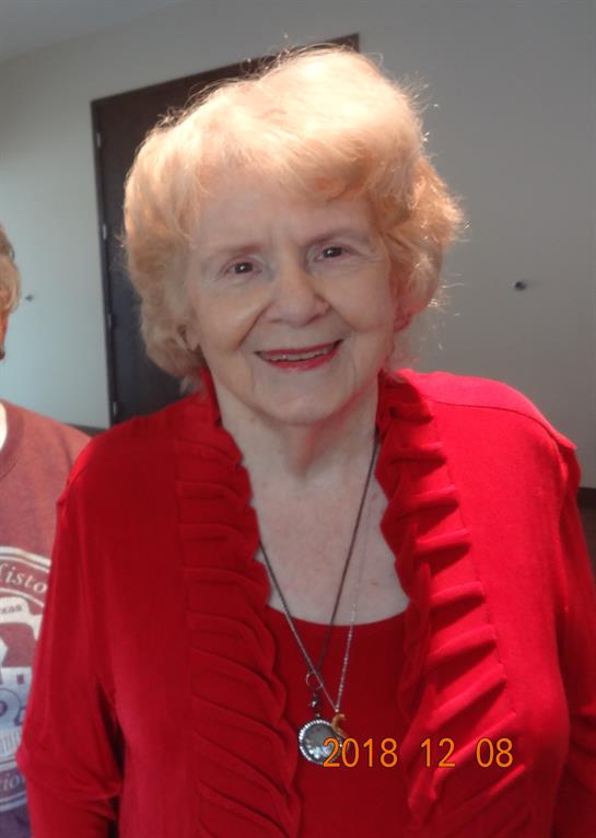 A cheerful older woman wearing a bright red outfit shares a joyful moment at a community gathering.