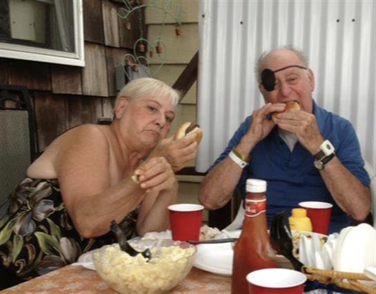A couple relaxes outdoors, savoring grilled food and drinks during a sunny afternoon.