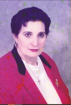 An elderly woman dressed in a red blazer and white blouse poses confidently while wearing earrings.