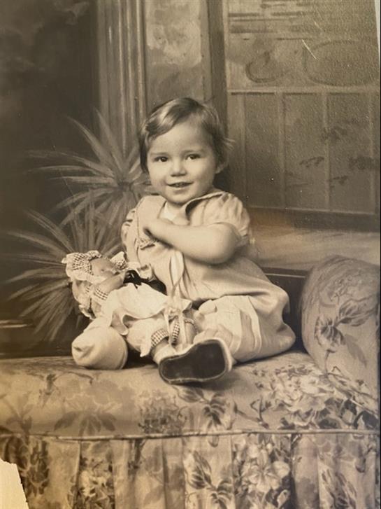 A joyful child sits on a floral couch, hugging a doll with a charming smile in an elegant room.