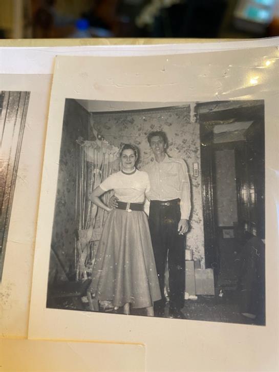 A couple stands confidently in a charming living room filled with vintage decor.
