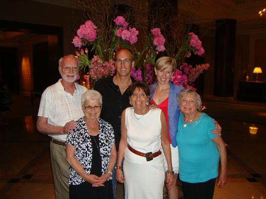 Group of six people posing together by a colorful flower arrangement at a summer event.