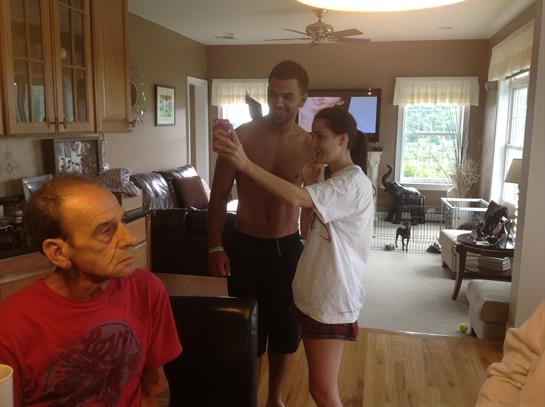 Two friends pose for a selfie while another relaxes in the background in a bright living room.