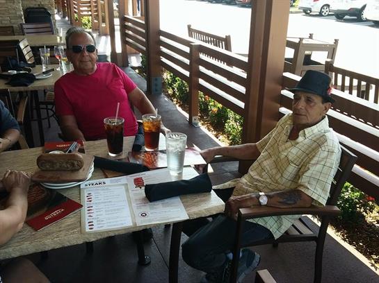 Two elderly friends relax and chat while enjoying lunch at an outdoor restaurant.