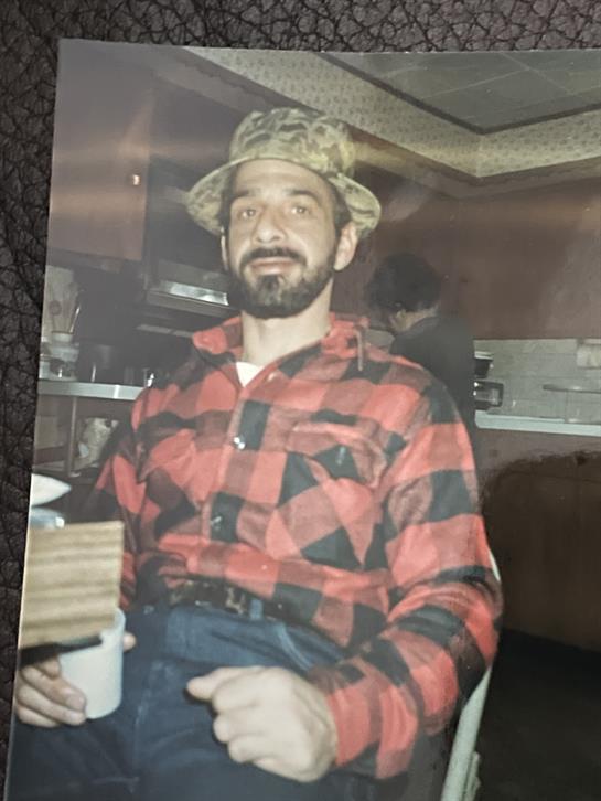 A man in a plaid shirt and hat sits comfortably, smiling in a cozy atmosphere.