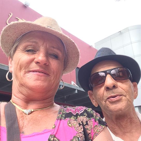 Elderly couple takes a joyful outdoor selfie, smiling and wearing hats.