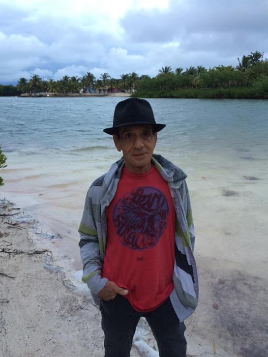 A young man poses on the sandy beach by the water, enjoying the scenery and gentle waves.