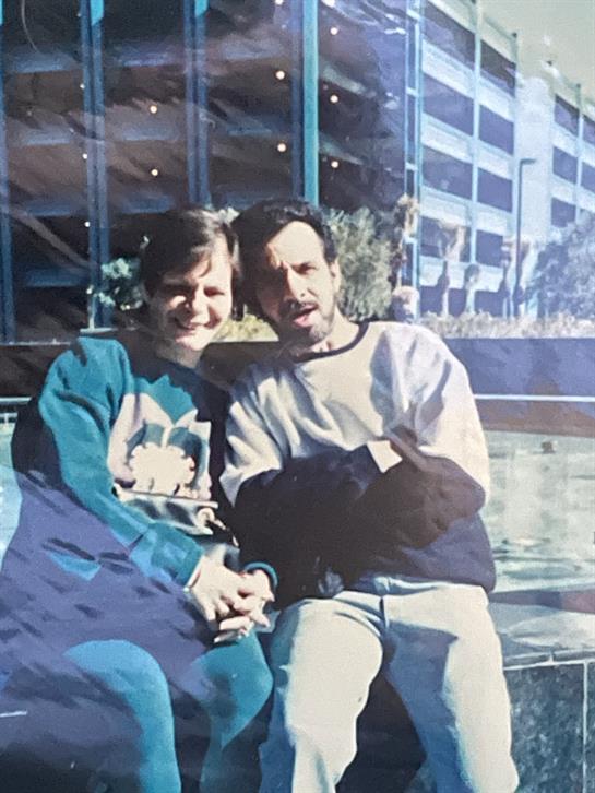 Two individuals relax together outside a bright, contemporary building on a sunny day.