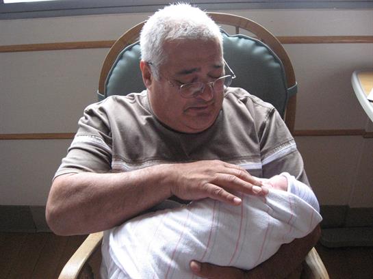 A grandfather gently holds his newborn grandchild, expressing deep affection in a hospital setting.