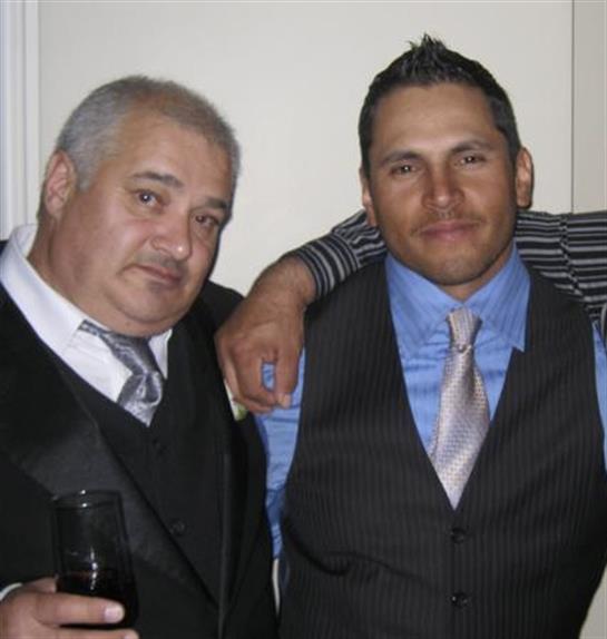 Two men in elegant outfits smile and pose with drinks at a festive gathering.